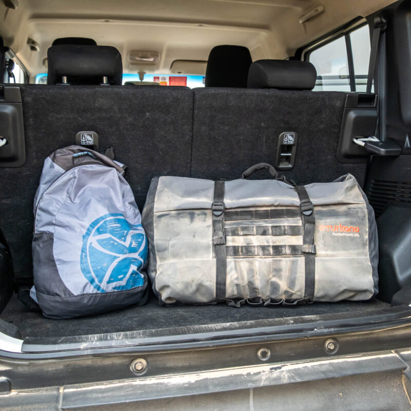 Turkana TurtleTrunk Stuff Bag packed in the rear cargo area of a white 4x4 vehicle, showing rugged overland travel and outdoor gear setup.
