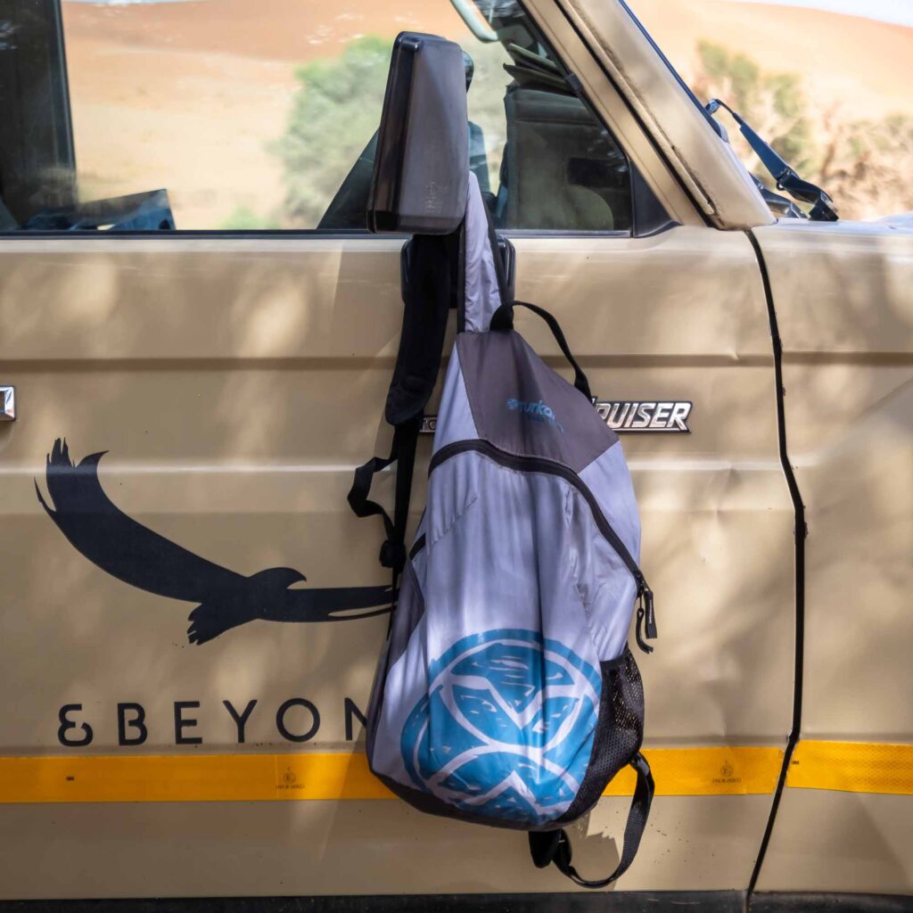 YakSak 15L packable daypack hanging from a Toyota Land Cruiser door in a desert setting.
