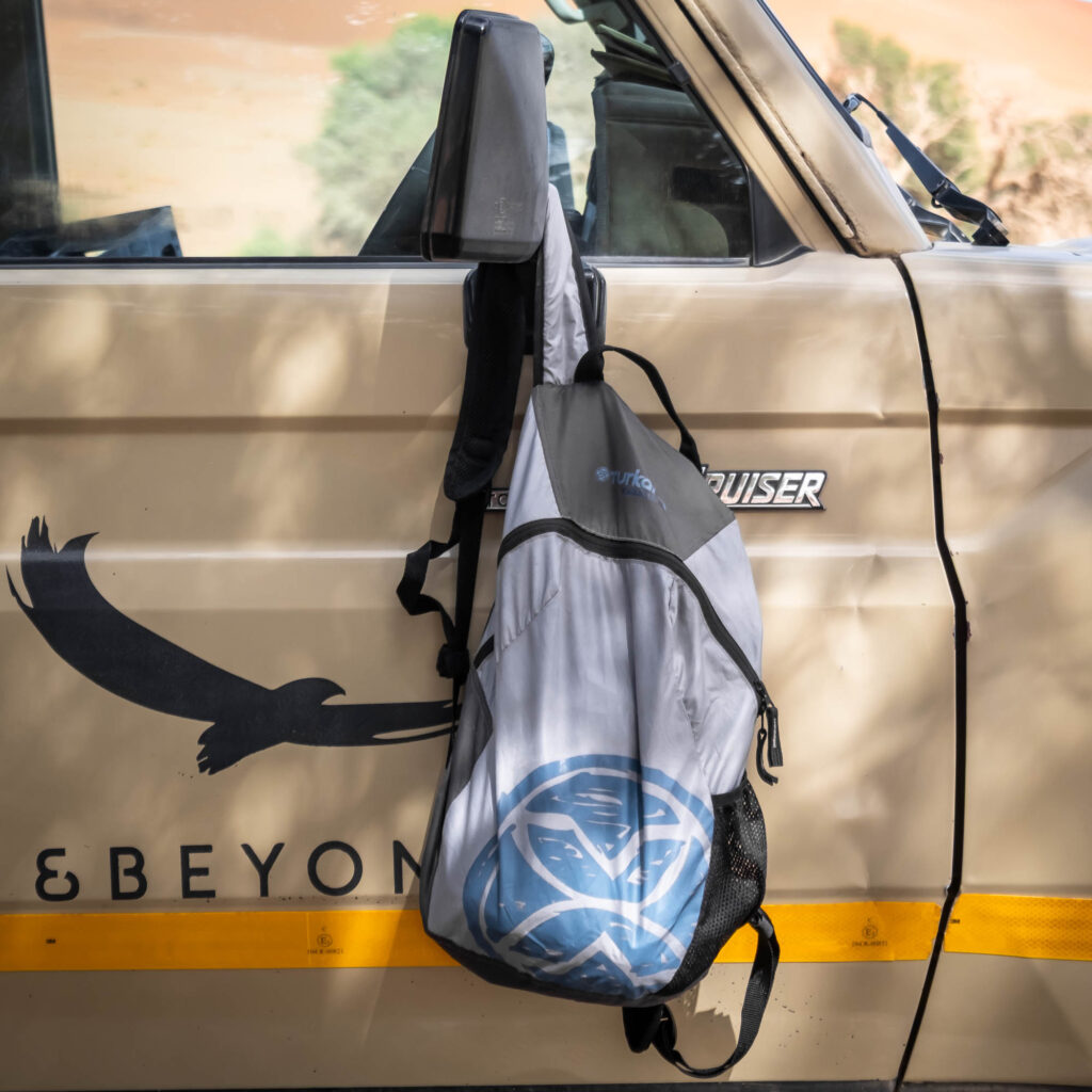 YakSak 15L packable daypack hanging from a Toyota Land Cruiser door in a desert setting.