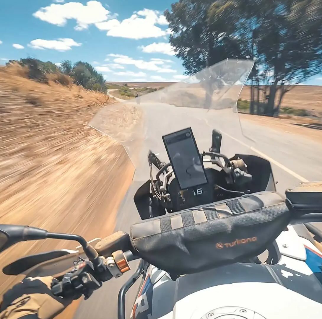 Rider’s view from an adventure motorcycle travelling on a rural road with a handlebar bag and mounted phone.