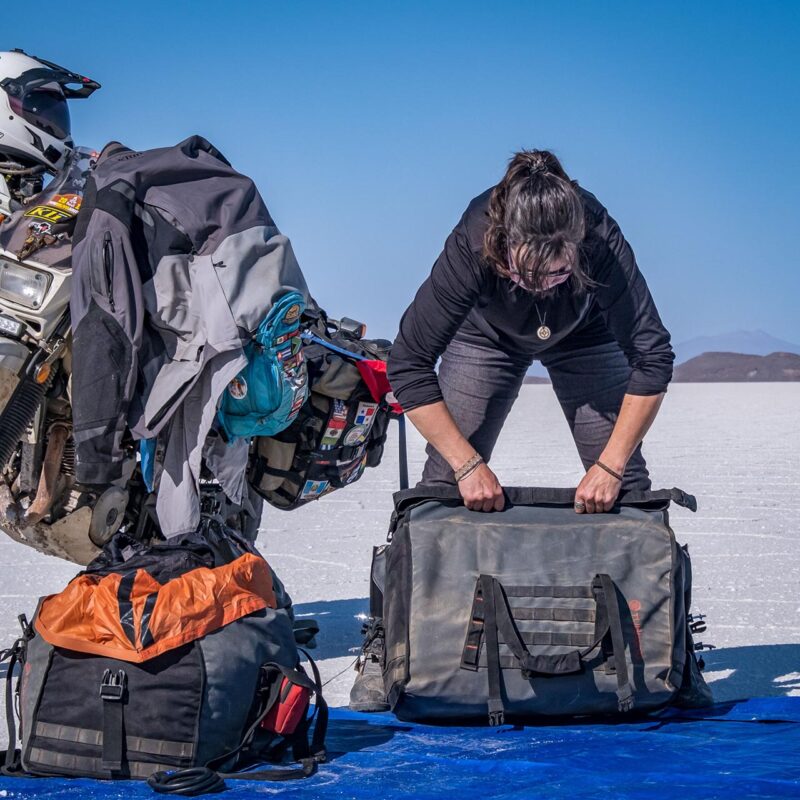 Rider folding the Turkana Duffalo duffel bag at a dusty camp on a rugged motorcycle adventure in Bolivia.