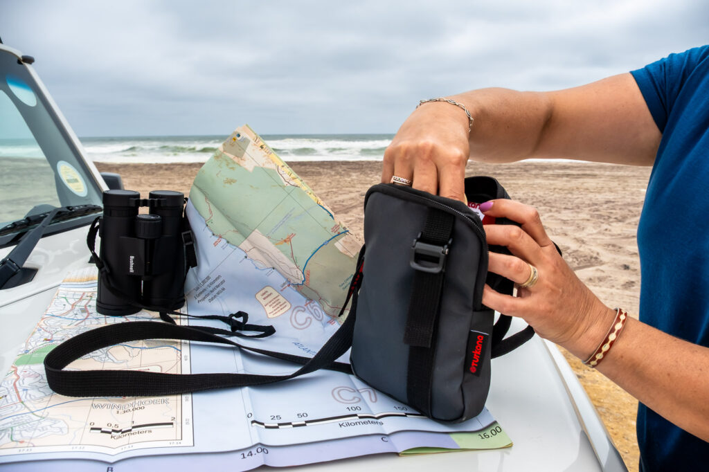 Turkana EDC Sling Thing resting on a Namibia road map and 4x4 bonnet, next to binoculars. Showcasing its tough travel design, ideal for overlanding, navigation, and everyday organisation.