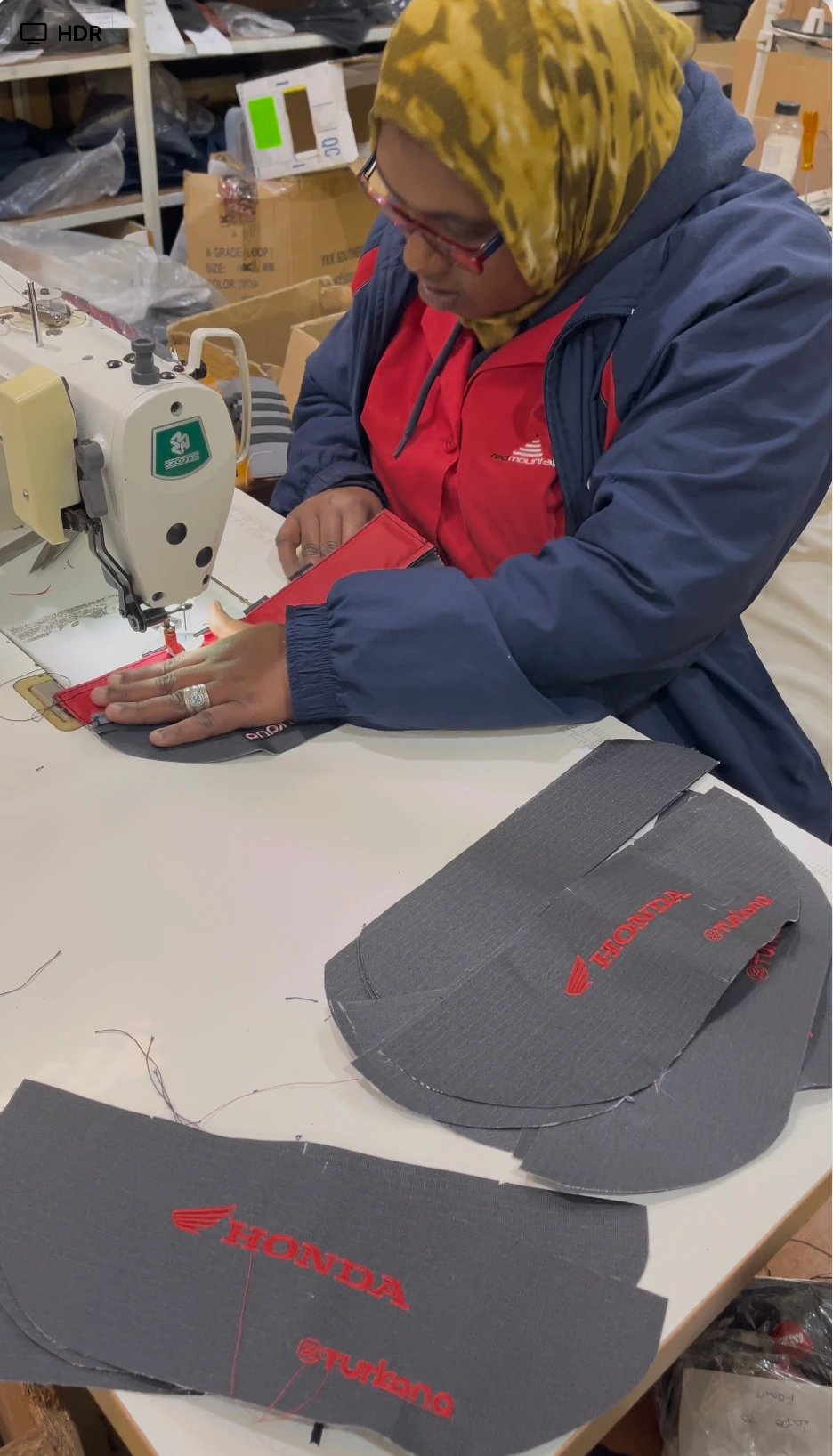 Sewing machinist stitching red and grey Honda and Turkana motorcycle luggage panels on an industrial machine.